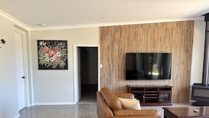 A modern living room with a brown leather sofa, a flat-screen TV, and a wood-paneled wall. - Modern Luxe Bush Retreat | 3BR Near Trails (Nannup)
