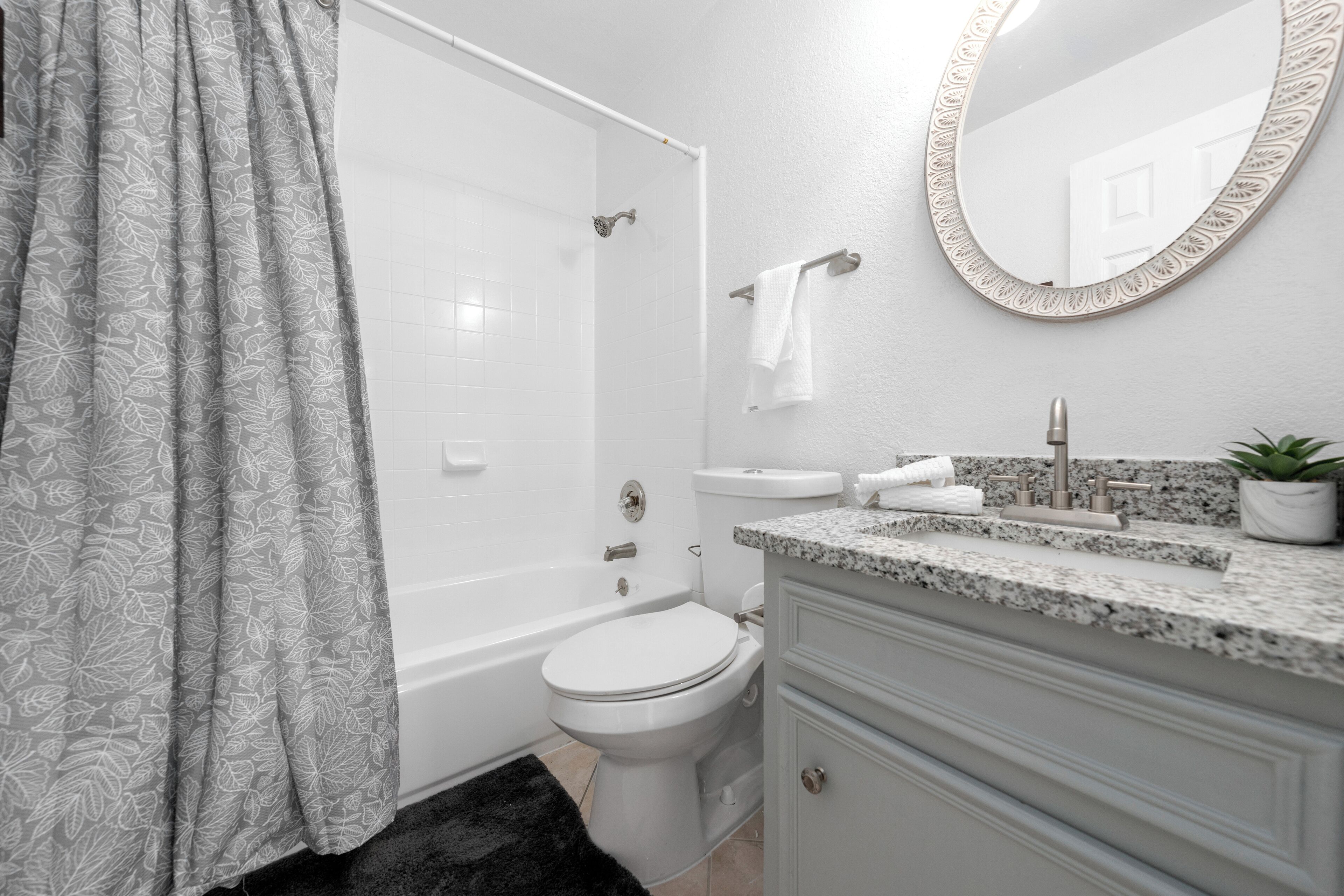 A bathroom with a shower, toilet, sink, and a mirror.