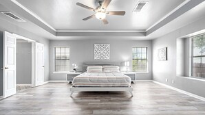 Un dormitorio con una cama centrada en la habitación, un ventilador de techo y una ventana con persianas.