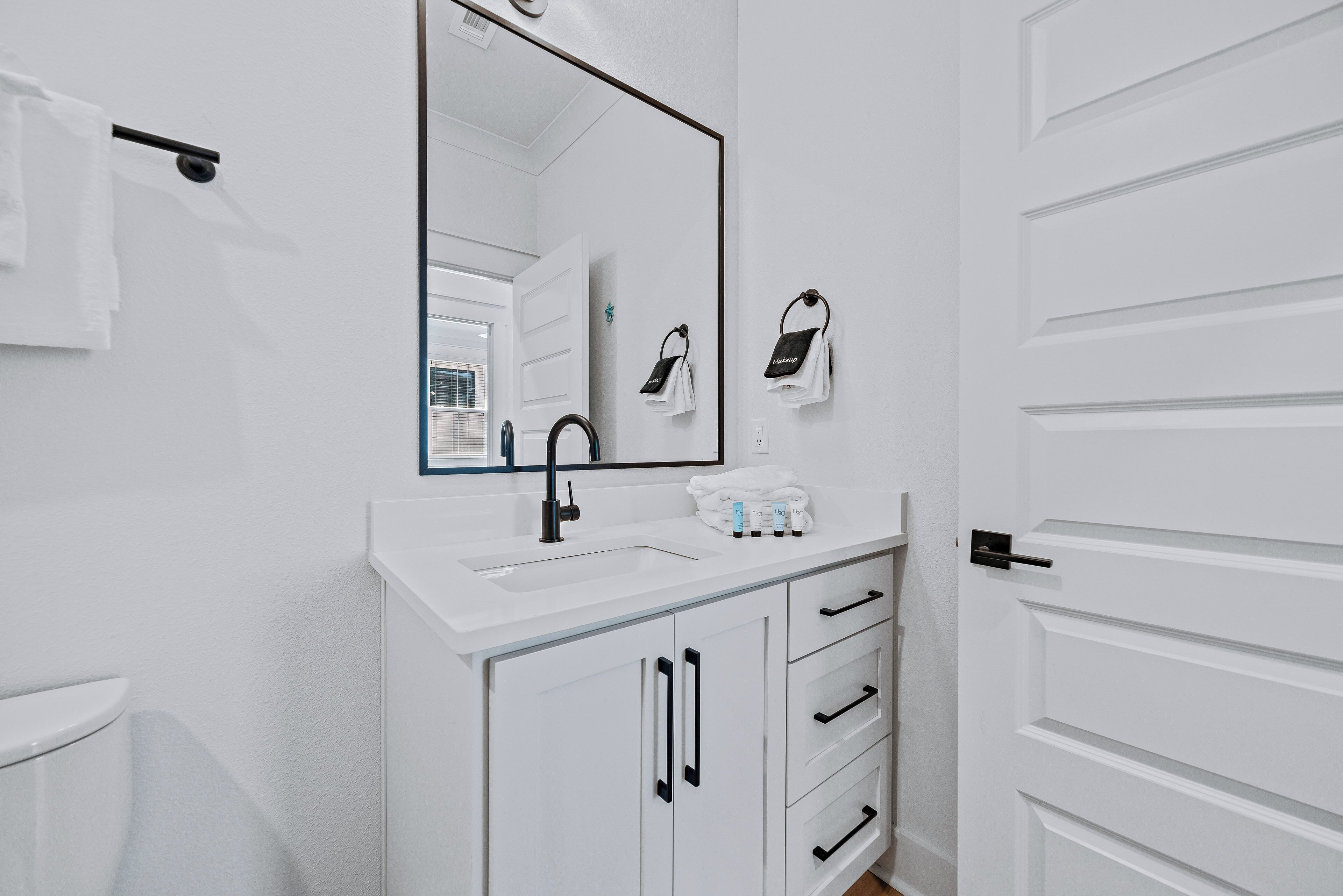 A bathroom with a white sink, black faucet, and a mirror above it. There are white towels hanging on a towel rack and a white door with a black handle.