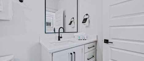 A bathroom with a white sink, black faucet, and a mirror above it. There are white towels hanging on a towel rack and a white door with a black handle.