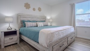 Une chambre à coucher avec un lit, des tables de chevet, un ventilateur de plafond et une fenêtre avec des stores.