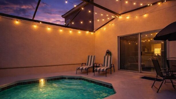 Un espace piscine sur le toit, avec un jacuzzi, deux chaises longues à rayures et des guirlandes lumineuses.