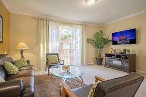 A living room with a leather sofa, glass coffee table, and a flat-screen TV mounted on the wall. - Spacious 3BR Townhouse in Vista Cay – Sleeps 8 Near Disney (Orlando)
