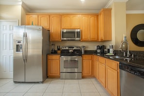 A kitchen with wooden cabinets, stainless steel appliances, and a tiled floor. - Spacious 3BR Townhouse in Vista Cay – Sleeps 8 Near Disney (Orlando)