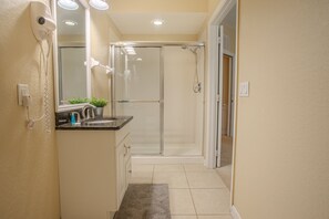 A bathroom with a shower, a sink, a mirror, and a hairdryer on the wall. - Spacious 3BR Townhouse in Vista Cay – Sleeps 8 Near Disney (Orlando)