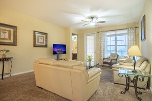 A living room with a beige sofa, a glass coffee table, a television, and a ceiling fan. - Spacious 3BR/2BA Apartment at Vista Cay, Minutes from Disney & Universal (Orlando)