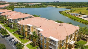 A multi-story hotel with a red-tiled roof, a parking lot, and a lake view. - Spacious 3BR/2BA Apartment at Vista Cay, Minutes from Disney & Universal (Orlando)