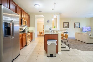 A modern kitchen with a refrigerator, microwave, and stove, a dining area with chairs, and a living room with a sofa and TV. - Spacious 3BR/2BA Apartment at Vista Cay, Minutes from Disney & Universal (Orlando)