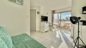 Ein Wohnzimmer mit Sofa, Fernseher, Schreibtisch und Balkon mit Aussicht.