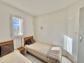 A small, clean room with two beds, a window, and a door. - CAP D'AGDE - Plage Richelieu / Réf 0260 (CAP D'AGDE)