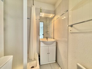 A bathroom with a white sink, mirror, and cabinet, a shower curtain, and a towel rack. - CAP D'AGDE - Plage Richelieu / Réf 0260 (CAP D'AGDE)