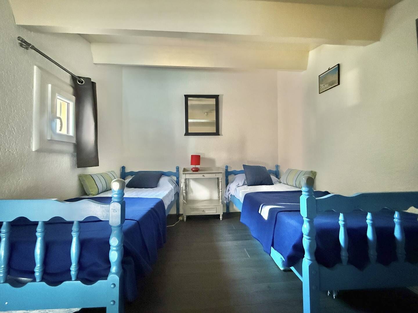 A room with two beds, each with a blue headboard and matching bedding. There is a nightstand with a lamp between the beds, and a mirror on the wall above the nightstand.