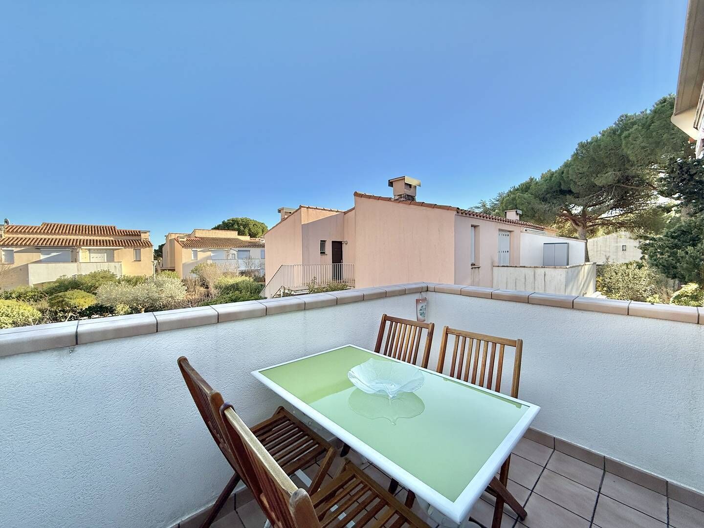 A rooftop terrace with a table and chairs, a clear view of neighboring buildings, and a tiled floor.
