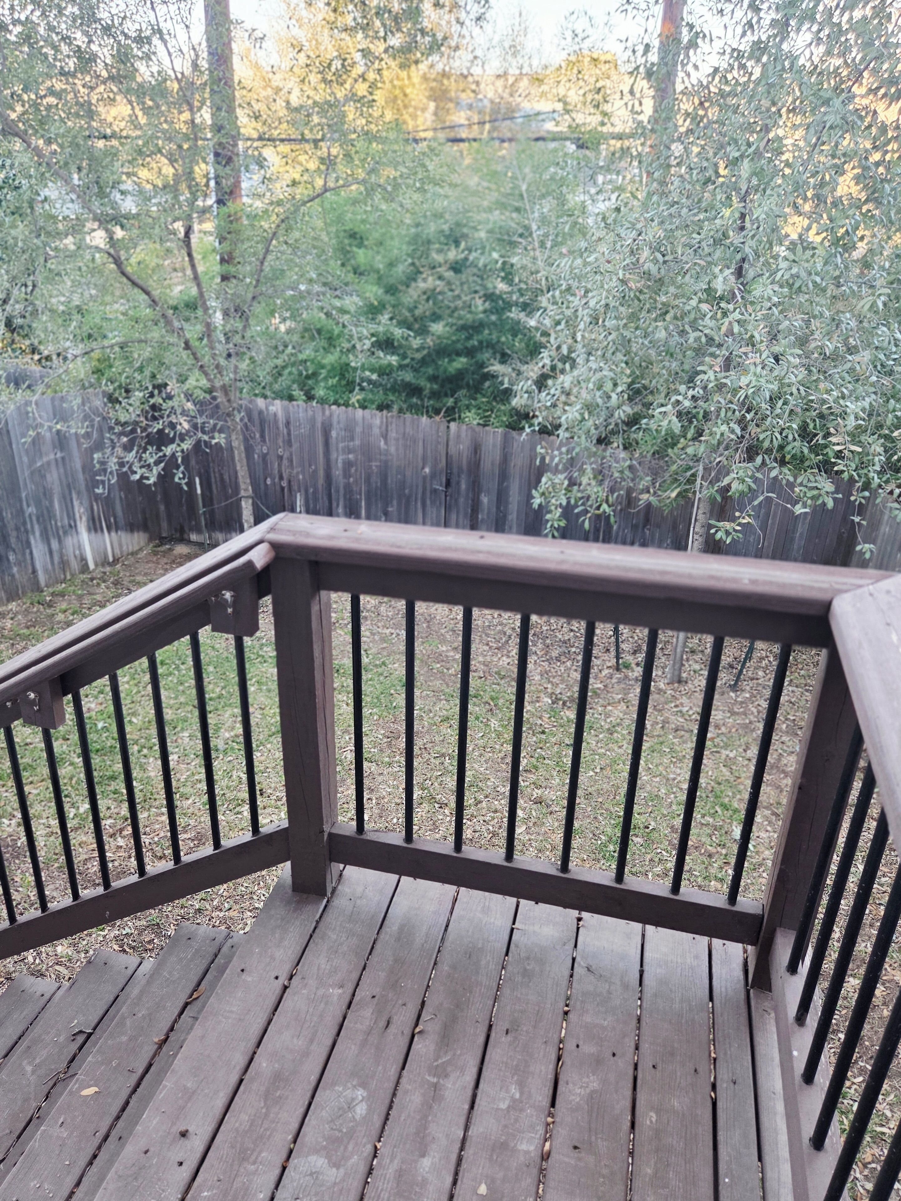 A wooden deck with a metal railing, surrounded by a wooden fence and trees.