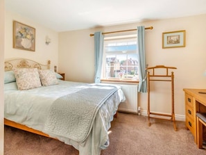 Une chambre à coucher comprenant un lit, un radiateur, une armoire en bois, une fenêtre avec des rideaux et un tableau accroché au mur.