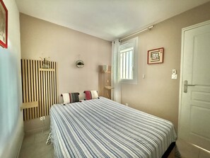 Ein Schlafzimmer mit Bett, Fenster, Tür und einer Wandablage mit Dekoration.