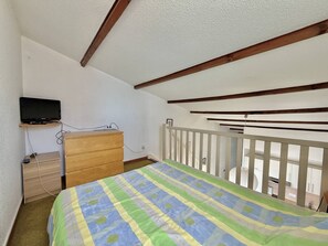 A bedroom with a bed, a dresser, a television on a shelf, and a balcony with a railing. - CAP D'AGDE - Plage du Môle / Réf 0197 (CAP D AGDE)