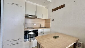 Una cocina compacta con armarios blancos, un horno de acero inoxidable y una mesa de madera.