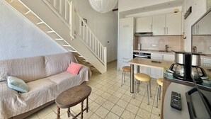Una cocina moderna con armarios blancos, un comedor con taburetes, un sofá con cojines y una escalera con barandillas blancas.