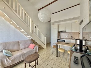 A modern kitchen with white cabinets, a dining area with stools, a sofa with cushions, and a staircase with white railings. - CAP D'AGDE - Plage du Môle / Réf 0197 (CAP D AGDE)