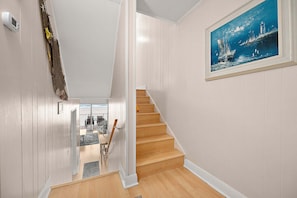 A staircase with wooden steps leading to a landing, white walls, and a framed painting of a seascape. - On Boardwalk - Oceanfront 2 Bed/2 Bath (Ocean City)