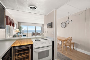 A compact kitchen with a stove, oven, and a dining area with a table and chairs. - On Boardwalk - Oceanfront 2 Bed/2 Bath (Ocean City)