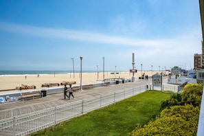 A boardwalk with benches and trash bins, overlooking a beach with people and a Ferris wheel in the distance. - On Boardwalk - Oceanfront 2 Bed/2 Bath (Ocean City)