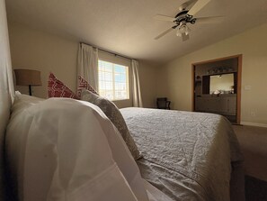 A bedroom with a bed, a ceiling fan, a window with curtains, a chair, and a dresser.