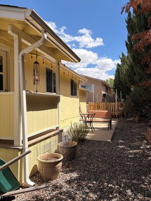 A yellow building with a covered patio area, outdoor seating, and a fenced garden.
