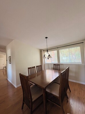 A dining room with a wooden table and chairs, a hanging light fixture, and a window with blinds.