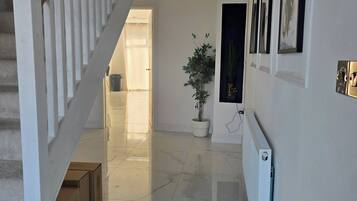 Un pasillo con piso de mármol, una escalera con barandillas blancas, una planta en maceta y cuadros en la pared.