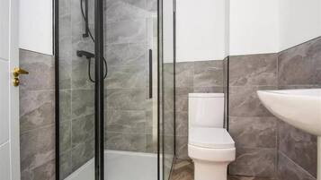 A modern bathroom with a glass-enclosed shower, a toilet, and a sink.