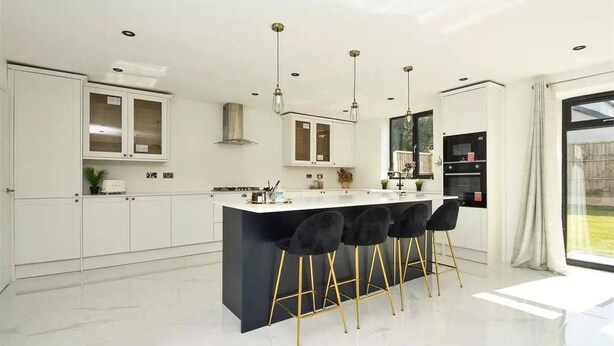 A modern kitchen with white cabinets, a black island, and gold bar stools. - Glams Beautiful Luxury Home (Wolverhampton)