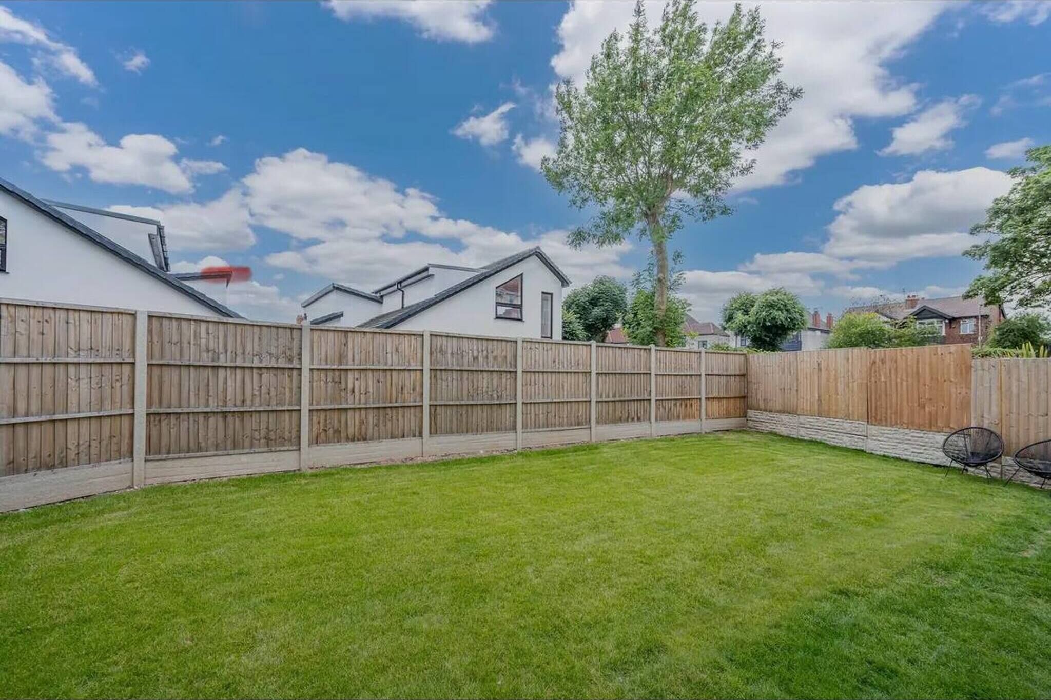 A backyard with a wooden fence, a lawn, and a tree.