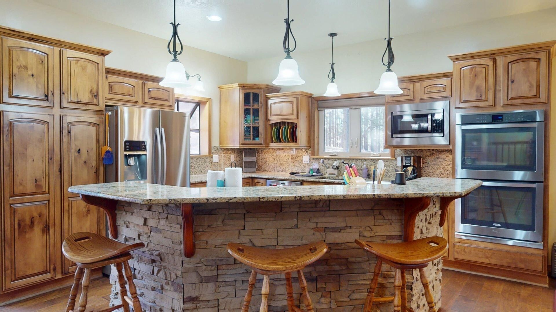 A kitchen with wooden cabinets, a granite countertop, a built-in island with stools, stainless steel appliances, and pendant lighting.