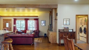 Ein gemütliches Wohnzimmer mit einem roten Ledersofa, einem Holzesstisch und einer Küchenzeile inklusive Waschmaschine.