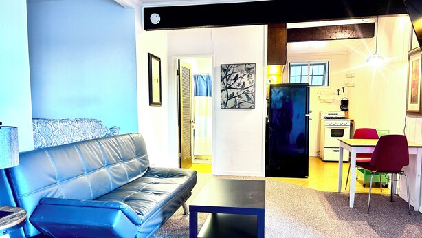 Ein Wohnzimmer mit blauem Sofa, einem kleinen Tisch und einer Küchenzeile mit Herd und Stühlen.