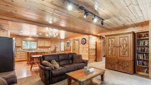 A cozy log cabin interior with a living room, kitchen, and dining area. - Adventure Creek Lodge | Hot Tub, Zipline & Kayaks (Island Park)
