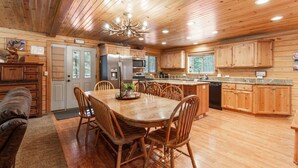 A spacious kitchen with wooden cabinets, a central island, and a dining area with chairs. - Adventure Creek Lodge | Hot Tub, Zipline & Kayaks (Island Park)