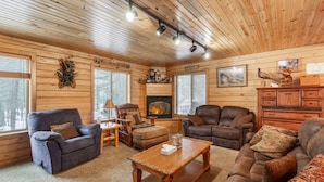 A cozy cabin interior with a fireplace, wooden walls, and a comfortable seating area. - Adventure Creek Lodge | Hot Tub, Zipline & Kayaks (Island Park)