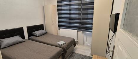 Un dormitorio pequeño y bien iluminado con dos camas, un armario, un radiador y un televisor.