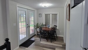 A kitchen with a refrigerator, a dining table with chairs, and a window with blinds.