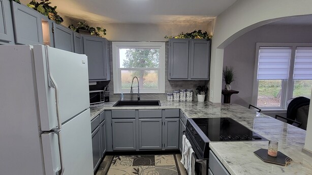 A modern kitchen with grey cabinets, a white refrigerator, a black stove, and a large window.