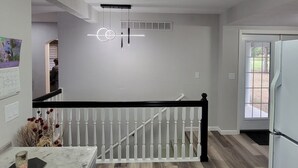 A modern kitchen with a wooden floor, a white railing, and a ceiling light fixture.