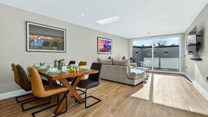 Ein modernes Wohnzimmer mit Essbereich, großen Fenstern und einem an der Wand befestigten Flachbildfernseher.