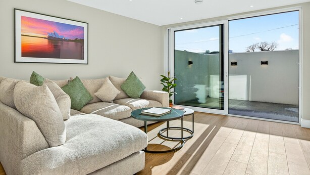 Ein modernes Wohnzimmer mit einem beigefarbenen Sofa, einem Glastisch und einem großen Fenster mit Blick auf ein Gebäude.