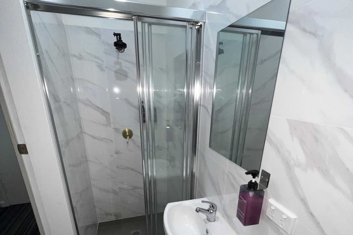 A bathroom with a glass-enclosed shower, a white sink, a mirror, and a soap dispenser.