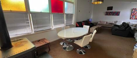 Una sala de estar moderna con una mesa redonda y sillas, un sofá, un sillón de masaje y un ventanal con persianas.
