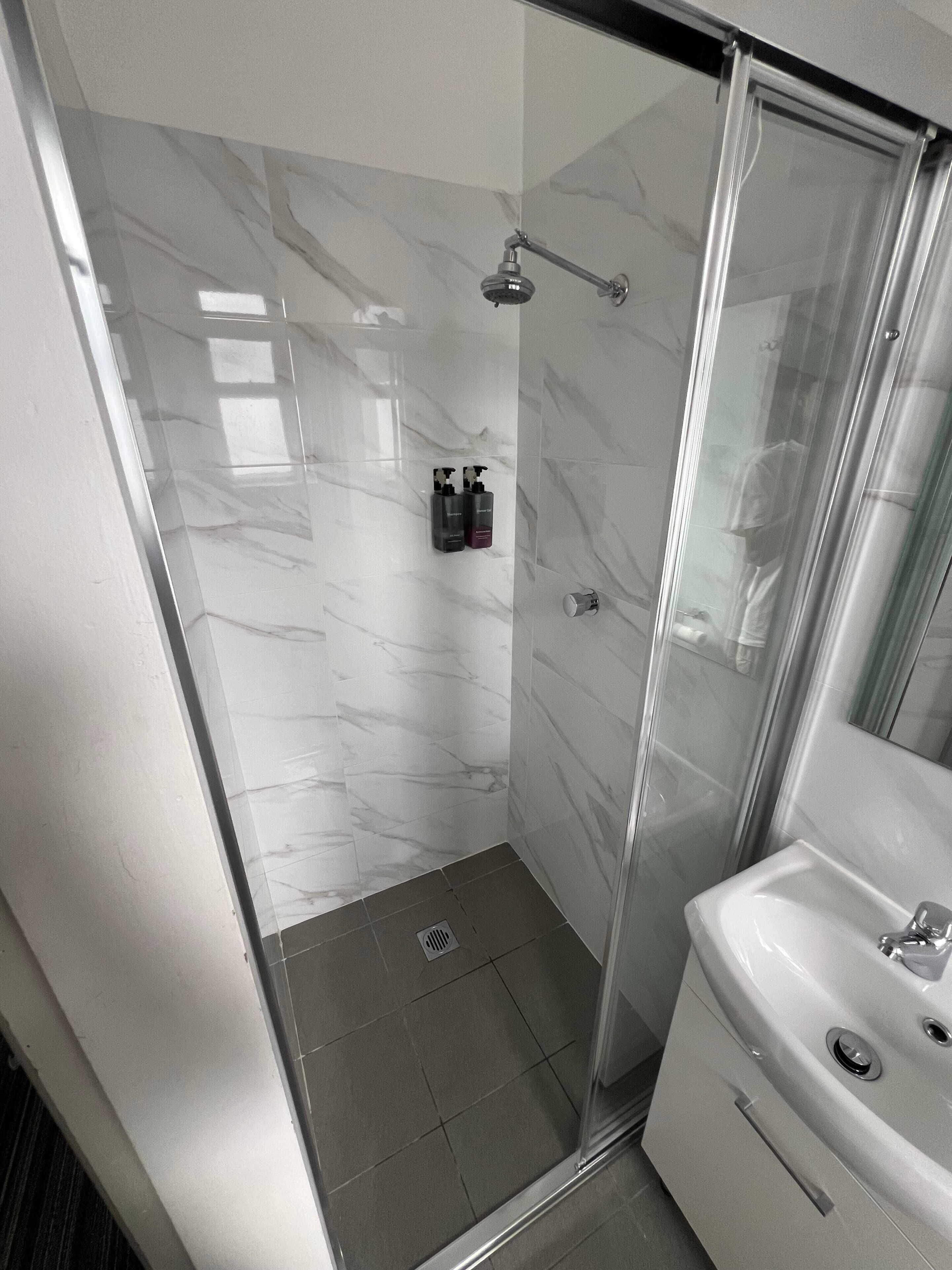 A modern bathroom with a glass-enclosed shower, a white sink, and marble walls.